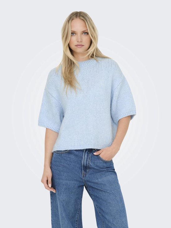 Femme aux cheveux blonds portant un pull tricoté bleu clair à manches courtes et un jean.