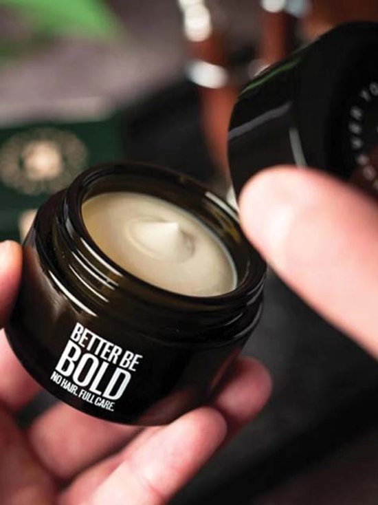 Een potje met de tekst "BETTER BE BOLD NO HAIR. FULL CARE." Een vinger houdt de open pot met witte crème omhoog.