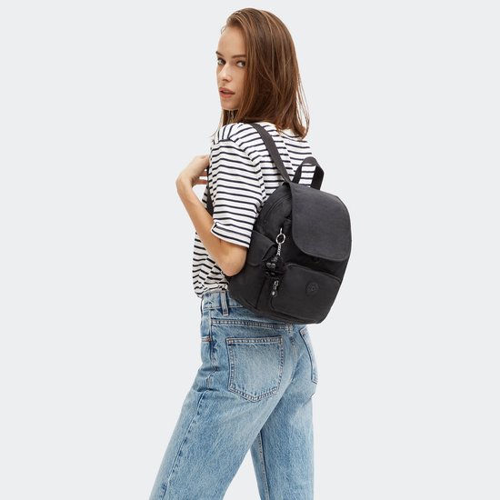 Vrouw met gestreept shirt en spijkerbroek draagt een zwarte Kipling rugzak.
