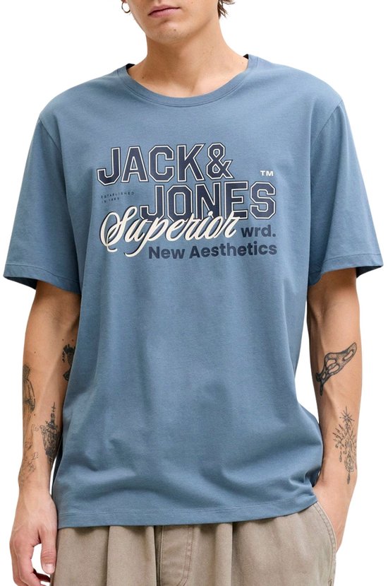 Homme avec des tatouages portant un t-shirt bleu Jack & Jones avec imprimé 'Jack & Jones Superior New Aesthetics'.