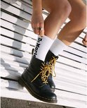 Mannequin portant des bottes Dr. Martens Pascal noires avec lacets jaunes et chaussettes blanches avec logo 'Dr. Martens'.