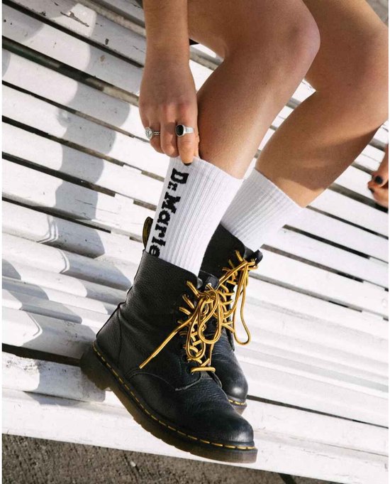 Mannequin portant des bottes Dr. Martens Pascal noires avec lacets jaunes et chaussettes blanches avec logo 'Dr. Martens'.