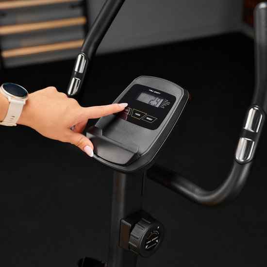 Close-up van een hand die het LCD-scherm van een hometrainer bedient.