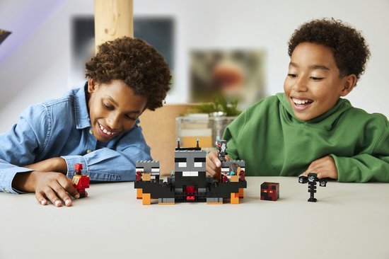 Deux garçons jouent avec un set LEGO Minecraft Wither Battle avec figurines et blocs de construction orange et gris.