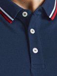 Man met een donkerblauwe polo met rode en witte strepen aan kraag en mouwen, lachend.