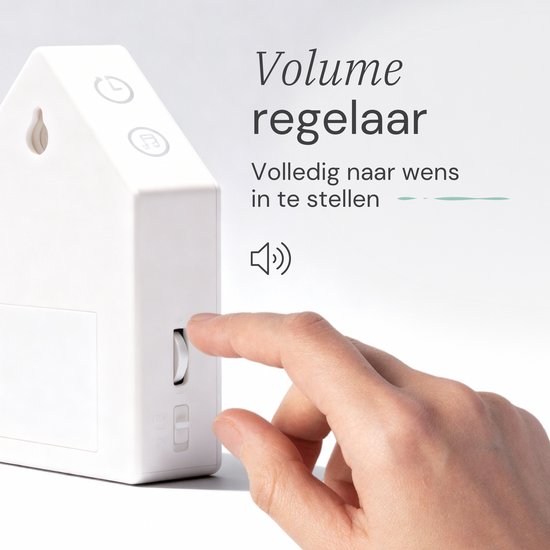 Vinger draait aan volumeregelaar op de witte achterkant van een huisvormig geluidshuisje. Tekst: 'Volume regelaar'.