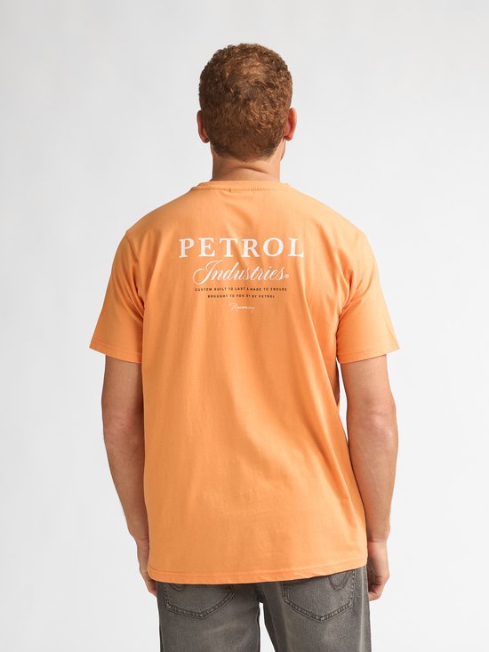 Man van achteren draagt een oranje t-shirt met "PETROL Industries" op de rug en een grijze jeans.