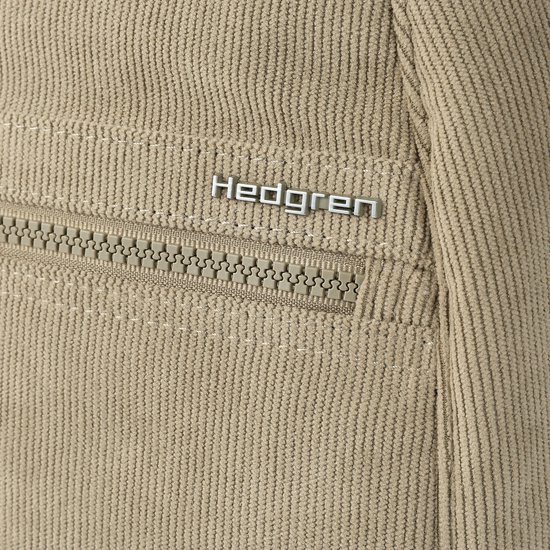 Close-up van het 'Hedgren'-logo op een beige ribfluwelen rugzak, met een rits.