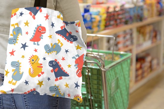 Une femme dans un magasin porte un sac blanc à motif de dinosaures et d'étoiles rouges, bleus et jaunes.