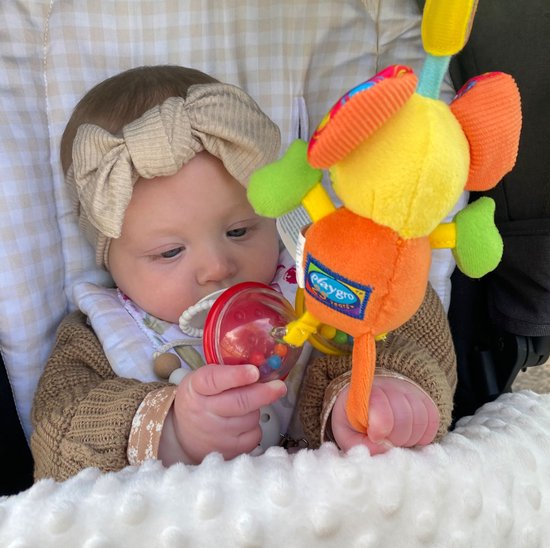 Een baby in een kinderwagen kijkt naar Mimsy de Muis, een gele knuffel met oranje lijf, groene armen en rode oren met stippen.