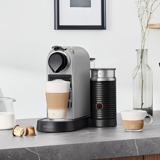Zilverkleurige Krups Nespresso Citiz & Milk machine in keukenomgeving met melkopschuimer, latte en capsules.