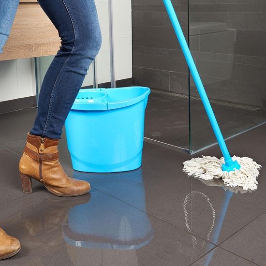 Onderlichaam van een vrouw met bruine laarzen en spijkerbroek, die de vloer dweilt met een blauwe mop en emmer in een badkamer.