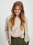 Een lachende vrouw met lang blond haar, draagt een beige vest over een bloemenblouse.