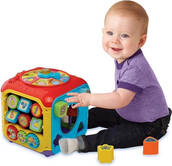 Een baby in een paars T-shirt speelt met een veelkleurige VTech activiteitenkubus met dierengeluiden en knoppen.