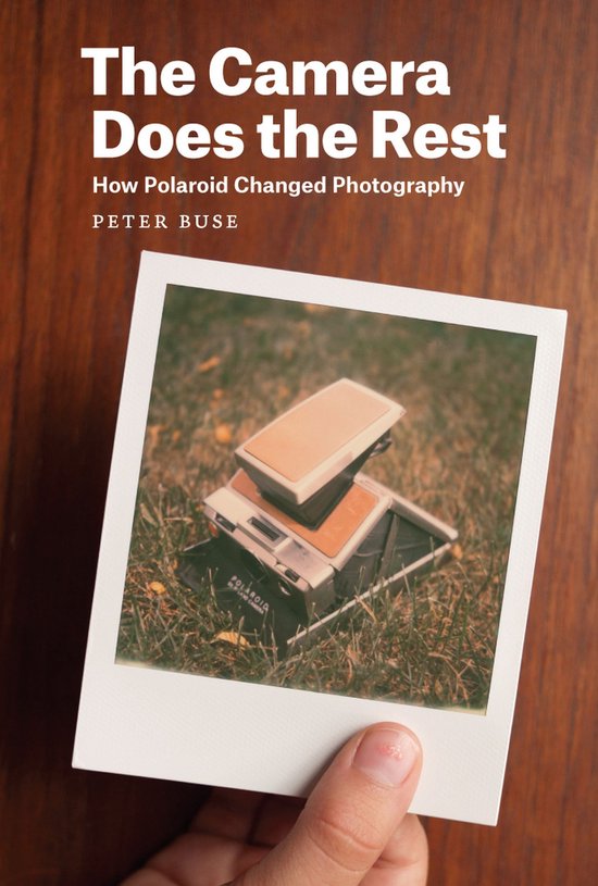 Boek kaft 'The Camera Does the Rest' met Polaroids en gras.