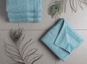 Deux serviettes bleu clair, une pliée et une à plat, sont posées sur un fond carrelé avec des plumes de paon.