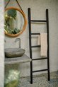 Zwarte decoratieve ladder met een beige geruite handdoek op de middelste sport, naast een wastafel.