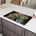 Een inductiebeschermer met een boeket bloemen, geplaatst op een wit aanrecht met donkere keukenkasten.