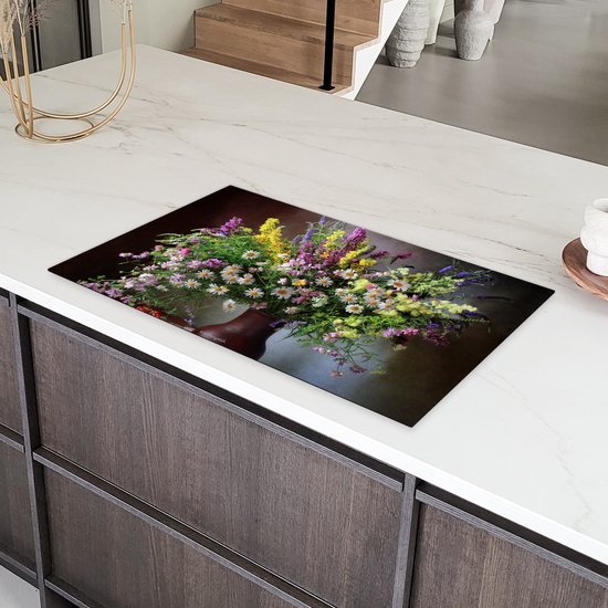 Een inductiebeschermer met een boeket bloemen, geplaatst op een wit aanrecht met donkere keukenkasten.