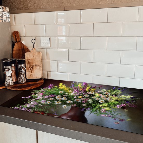 Een inductiebeschermer met een boeket bloemen, geplaatst op een donker aanrecht in een keuken met witte tegels.