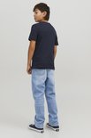 Jongen in donkerblauw T-shirt met print en lichtblauwe jeans. Draagt sneakers.