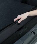 Hand rolt zwarte bumperbeschermer op in kofferbak van zilveren stationwagen.