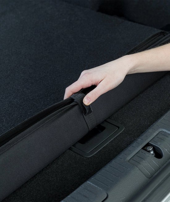 Hand rolt zwarte bumperbeschermer op in kofferbak van zilveren stationwagen.