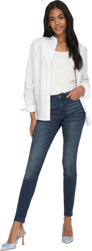 Model van achteren in een donkerblauwe skinny jeans met een witte blouse.