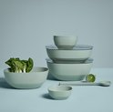 Groene serveerschalen, een grote schaal met bok choy, een kleine schaal, gestapelde schalen met deksels en een groene aubergine met een lepel.