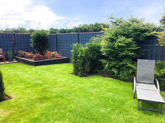 Een groen hekwerk met donkergrijs gaas en een houten plantenbak met rode en groene planten.