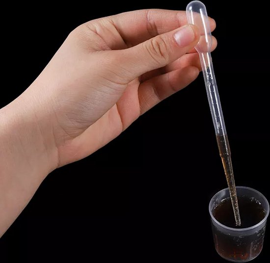 Une main tient une pipette en plastique remplie de liquide brun, au-dessus d'un petit gobelet en plastique contenant le même liquide.
